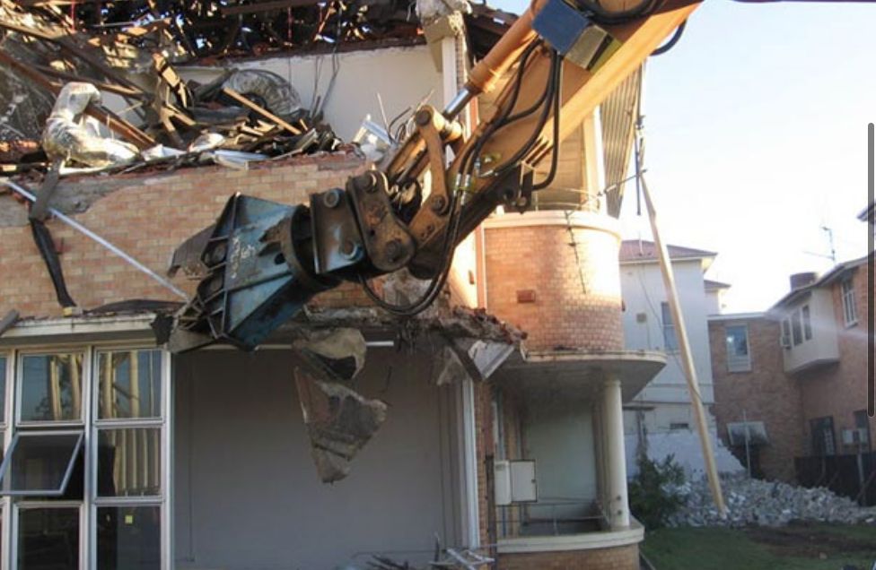 Excavator with a demolition claw tearing down a brick building