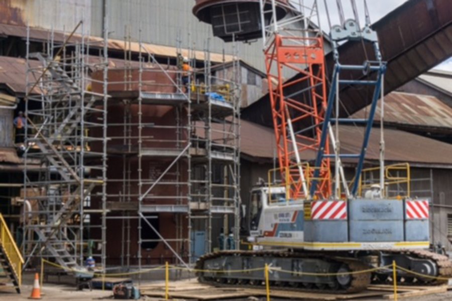 Scaffolding erected around an industrial tank with a crane working overhead
